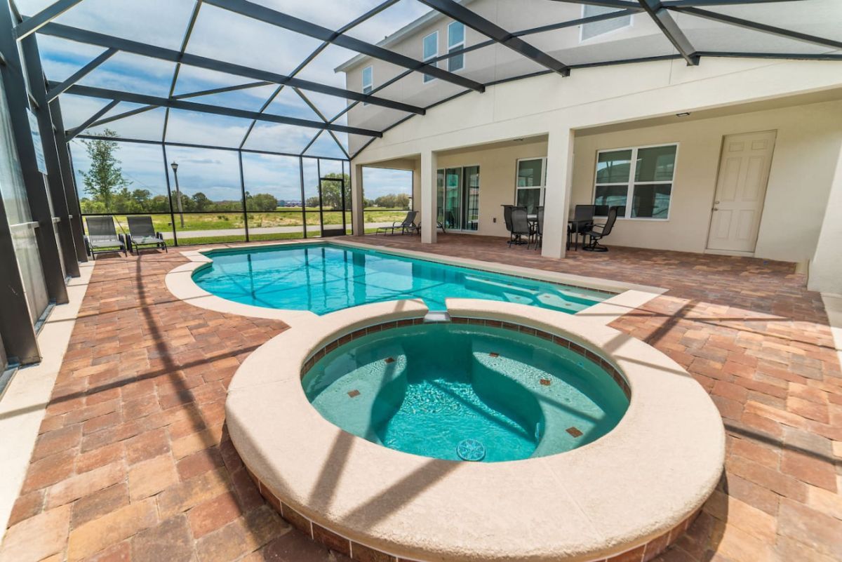 A screened-in swimming pool and integrated spa on a paved patio under a clear sky.
